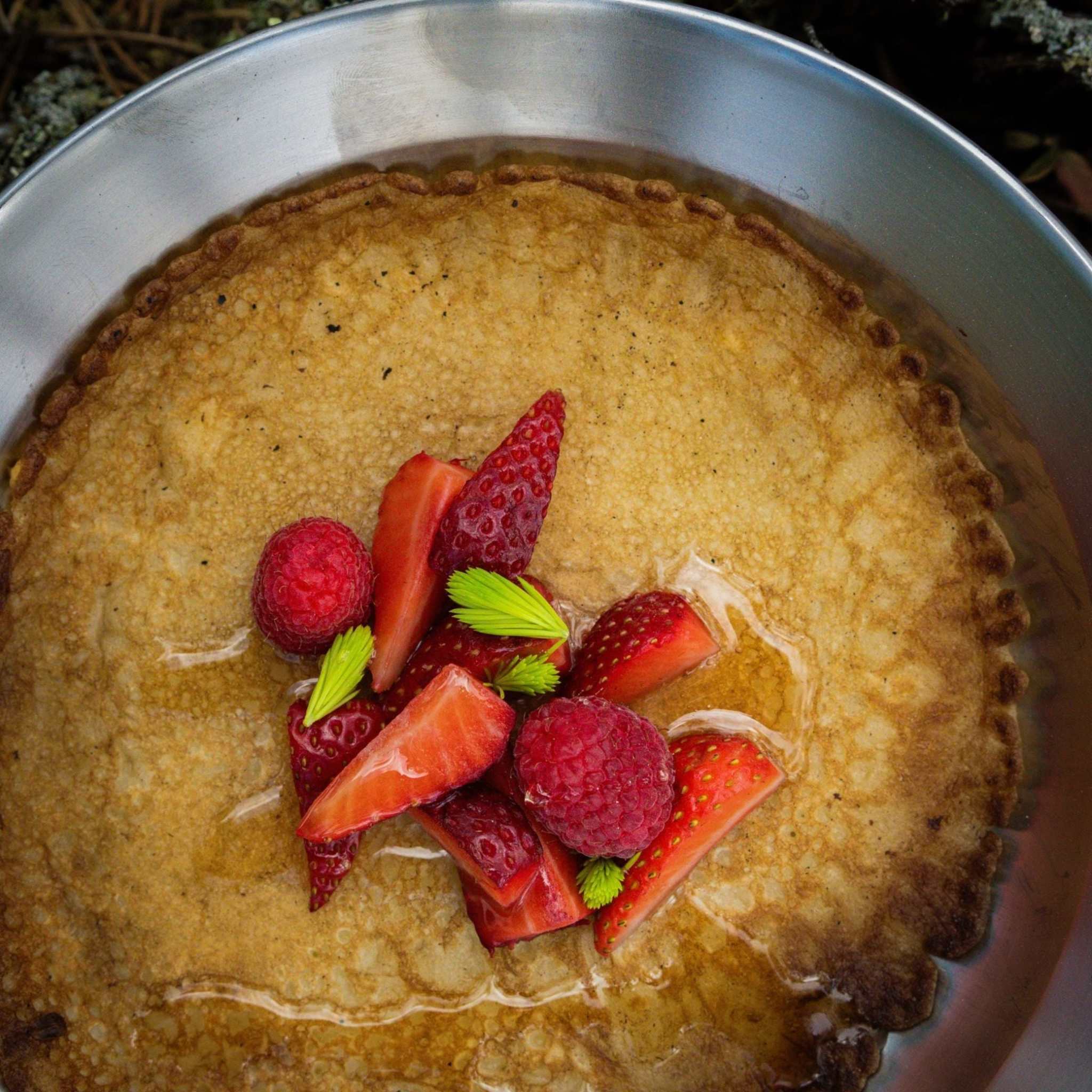 Pannkaku Vanilj med tunn, gyllenbrun pannkaka toppad med jordgubbar, hallon och gröna blad
