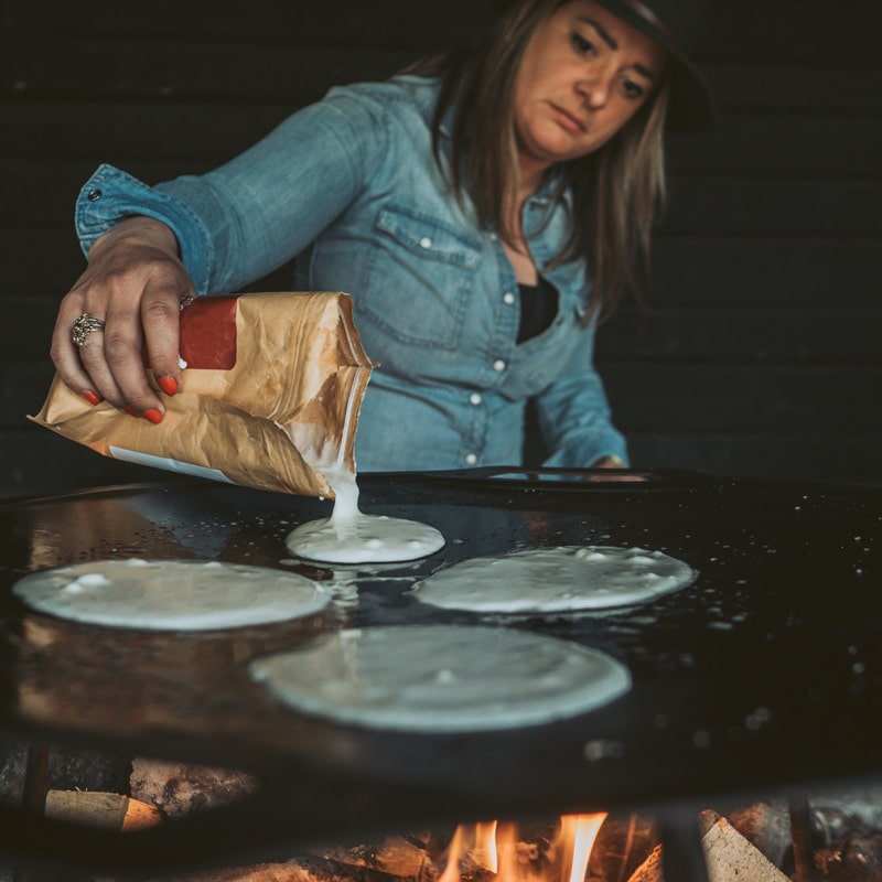 Pannkaksmix Pannkaku med Lingonsirap hälls ur brun papperspåse till tunna pannkakor på stekhäll.