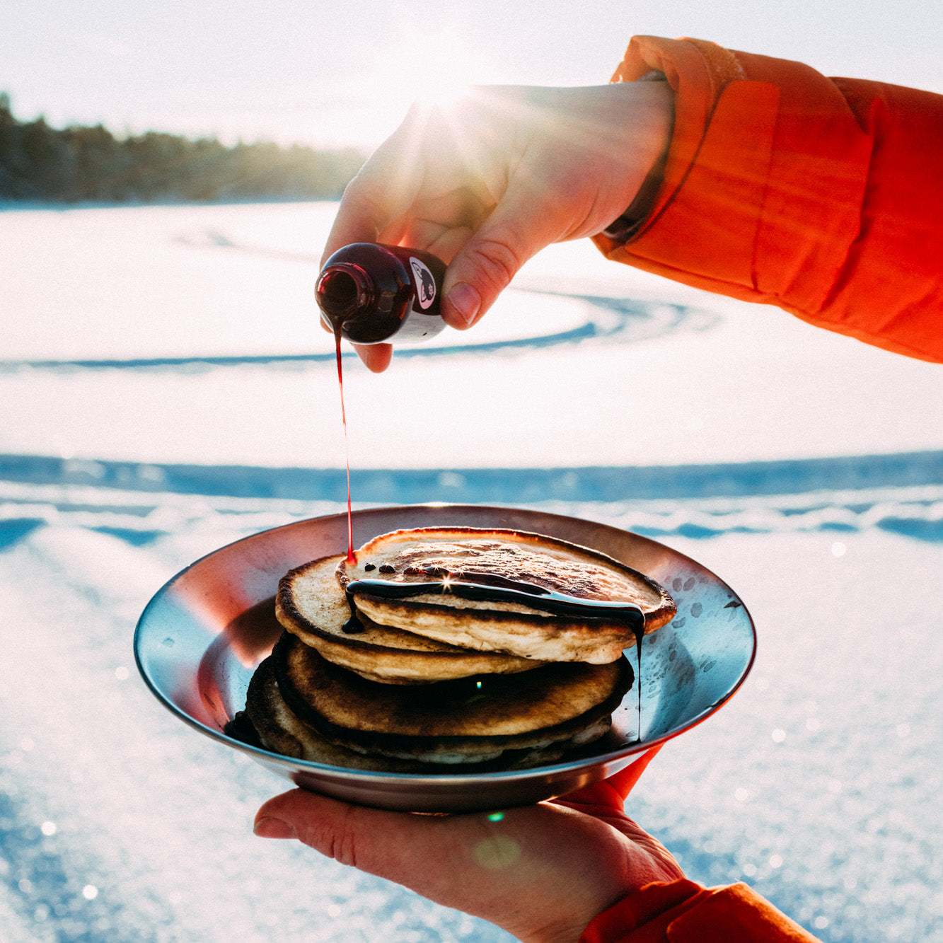 Pannkakor med gyllenbrun yta på tallrik, med lingonsirap ringlad över från en liten flaska; Pannkaku med Lingonsirap
