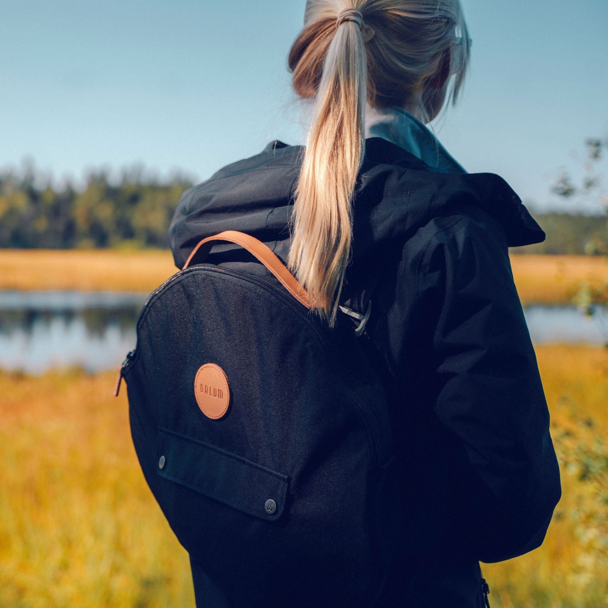 Ryggsäcksremmar Jälda i svart tyg med orange detalj, fästa på en ryggsäck med justerbar bärrem.