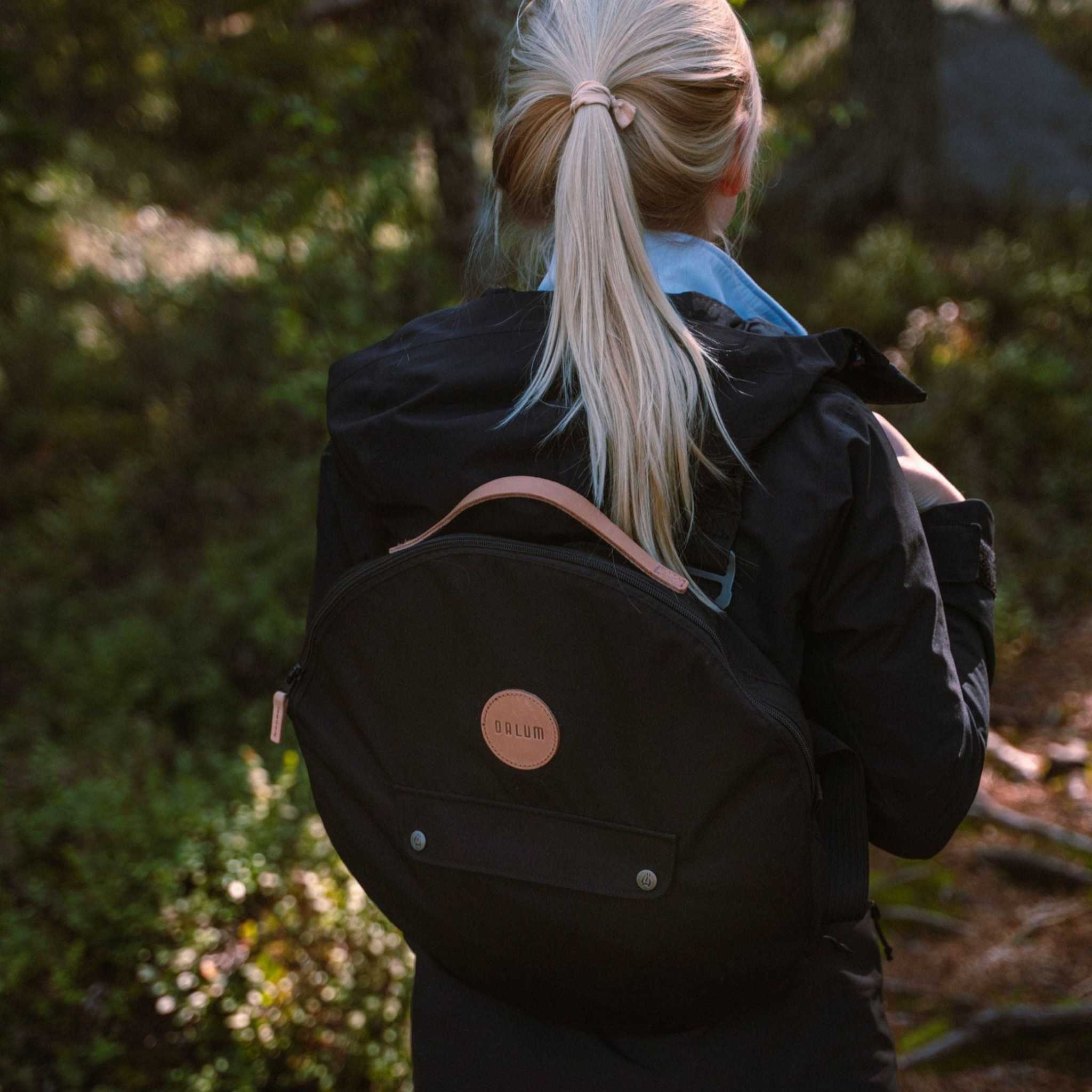 Stekhällsväska Jälda i svart slitstark textil med rundad form, bruna läderdetaljer och ytterficka med dragkedja.