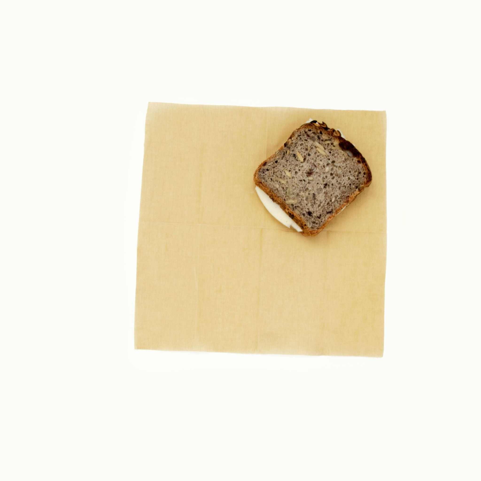 Bivaxduk i ljusgul, slät tygväv med en skiva grovt bröd placerad på duken.