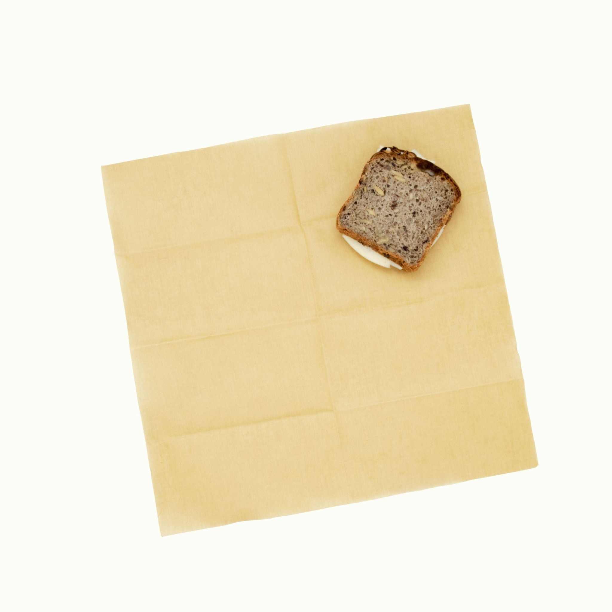 Bivaxduk i gulbeige vaxad tyg med slät yta och en skiva mörkt bröd placerad på duken.