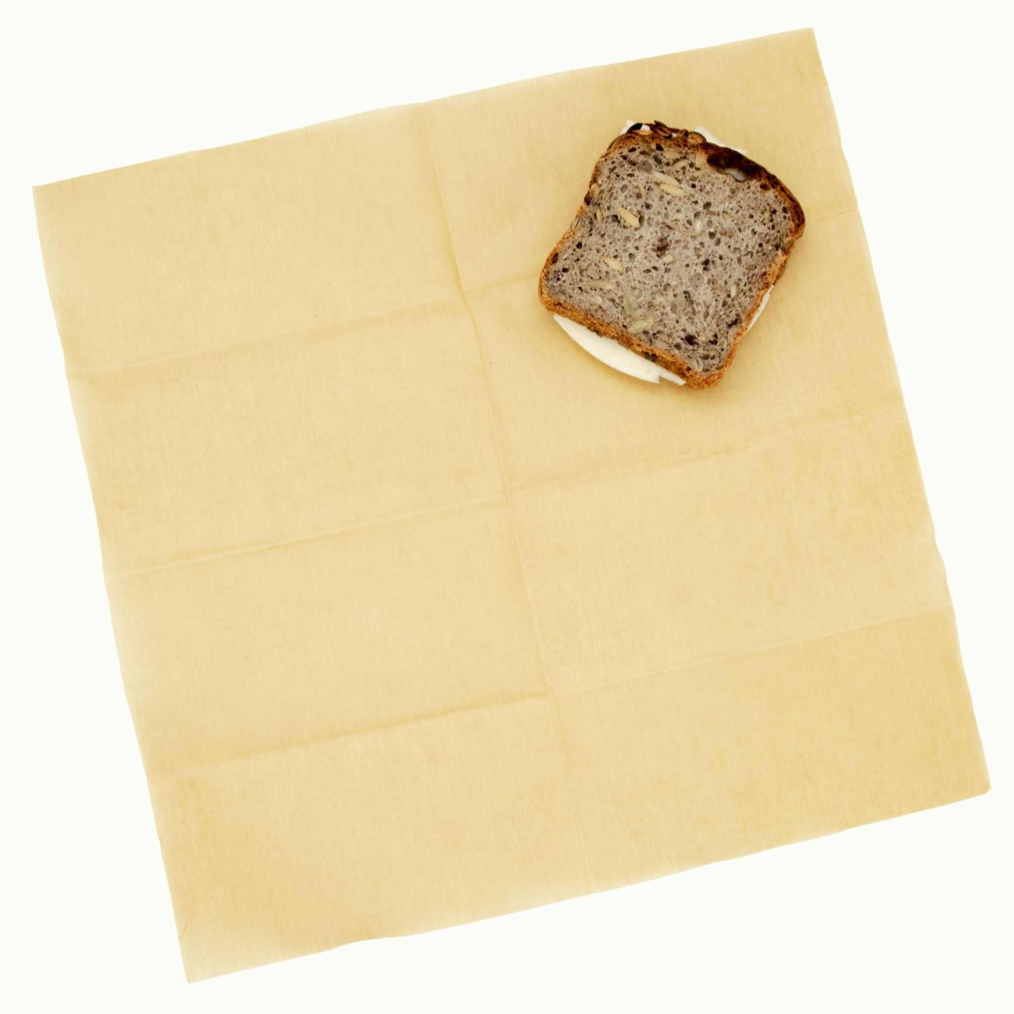 Bivaxduk i gulbeige bivaxbehandlad tygväv med diskret rutmönster, visad med en skiva grovt bröd.