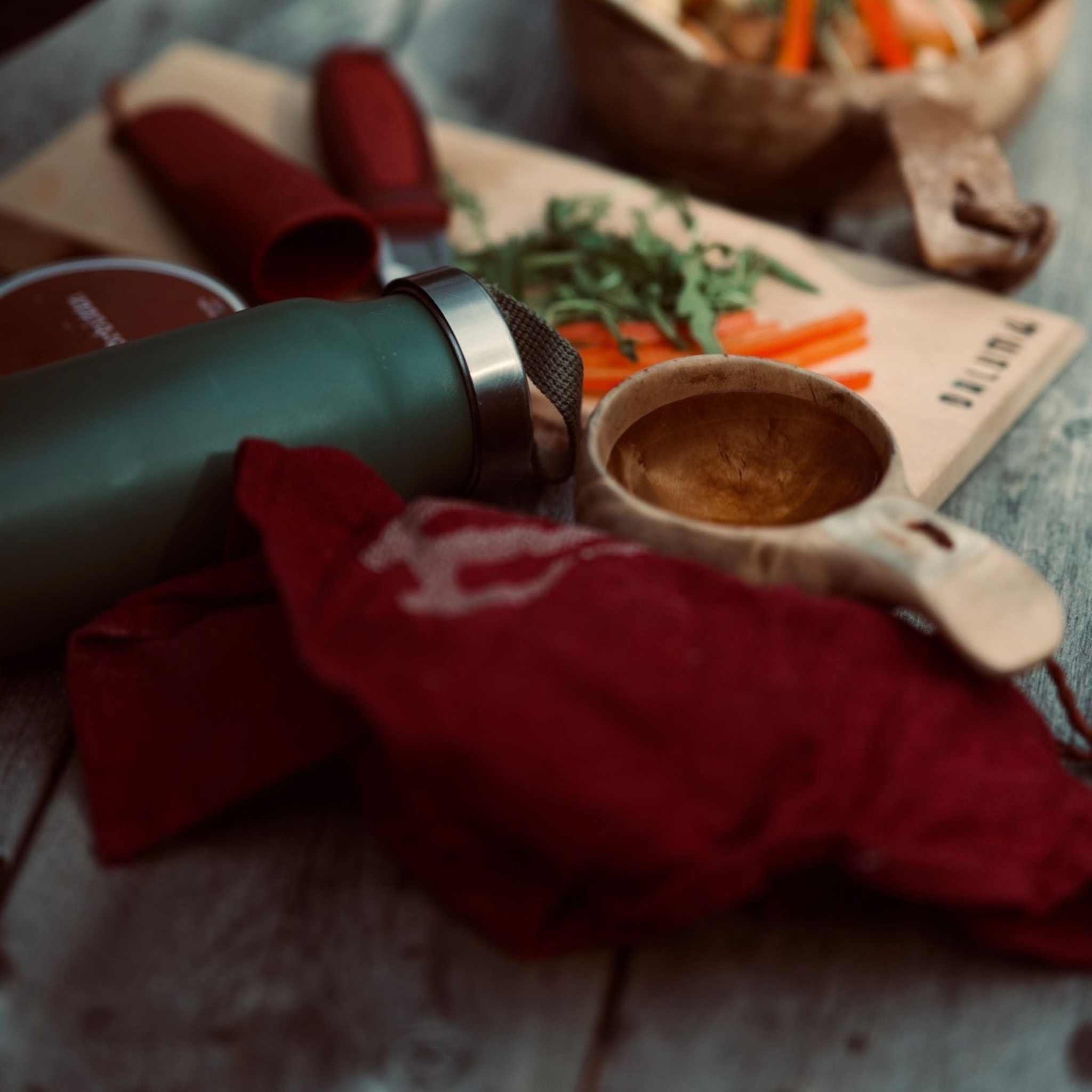 Linnehandduk outdoor i mörkrött linne med broderad ljus logotyp, vikt bland friluftskökets redskap.