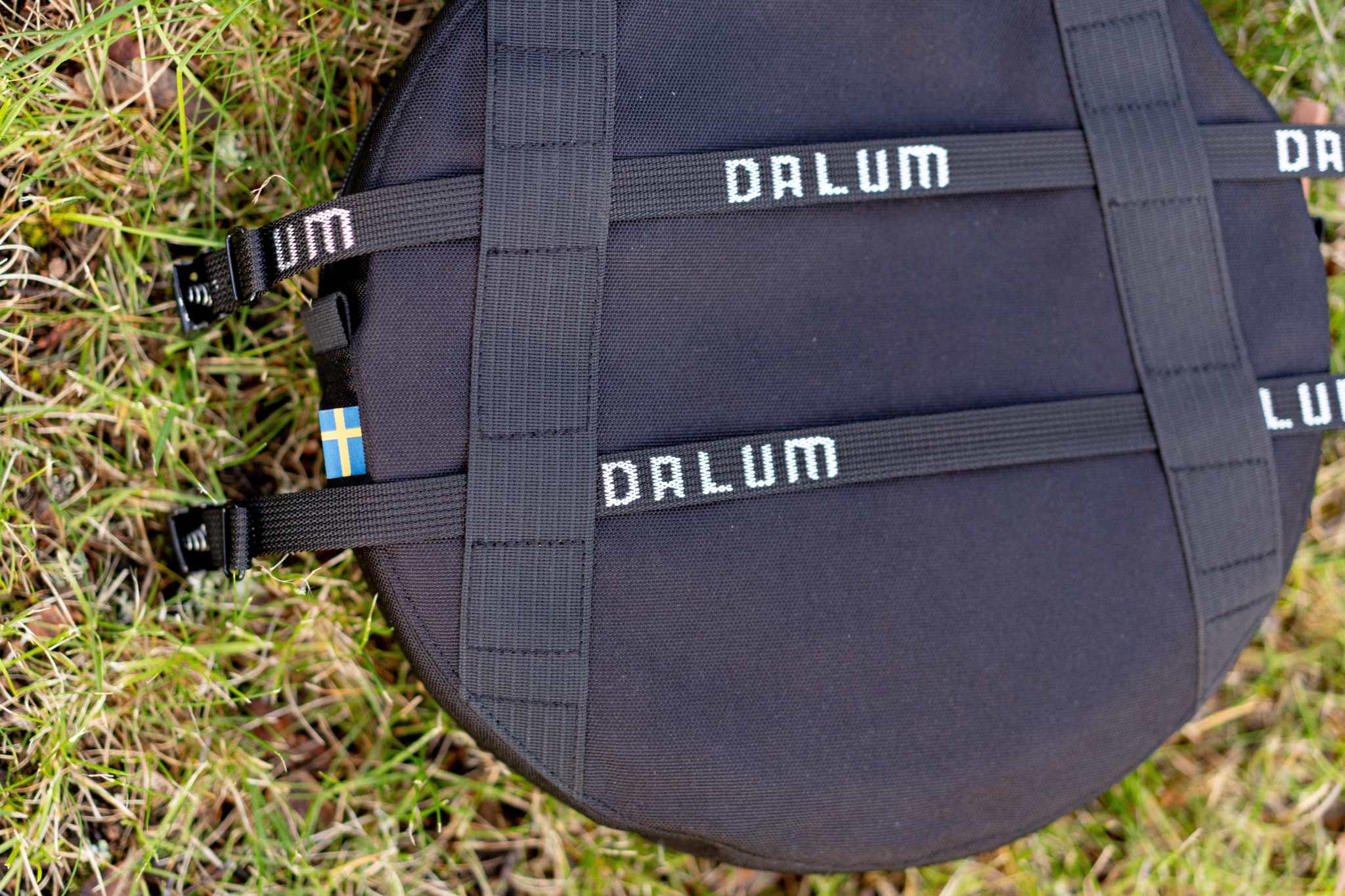 Spännremmar i svart polypropen med vita DALUM-logotyper och kraftiga spännen, fästa runt en rund väska.